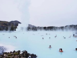 Mensen baden in een melkblauwe geothermische lagune met opstijgende stoom en heuvels in de verte bij de Blue Lagoon in IJsland