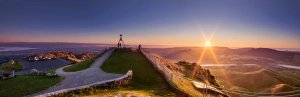 Panoramisch uitzicht bij zonsopgang of zonsondergang vanaf een heuveltop met mensen bij een monument en uitzicht over een uitgestrekt goudkleurig landschap met heuvels en een rivier in een natuurgebied