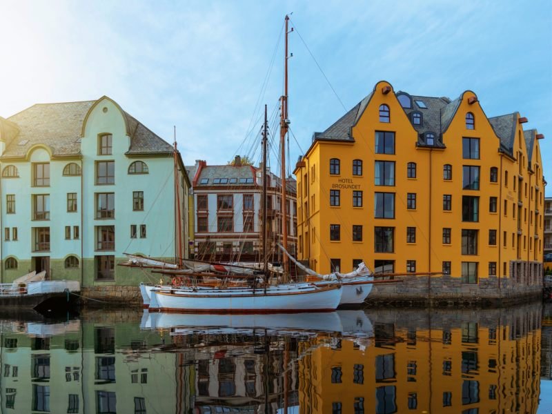 Colorful buildings and sailboats reflected in a calm harbor.
