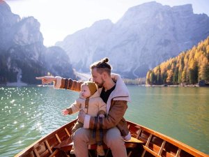 Man houdt een baby vast in een boot en wijst over een bergmeer met herfstbomen in een natuurgebied