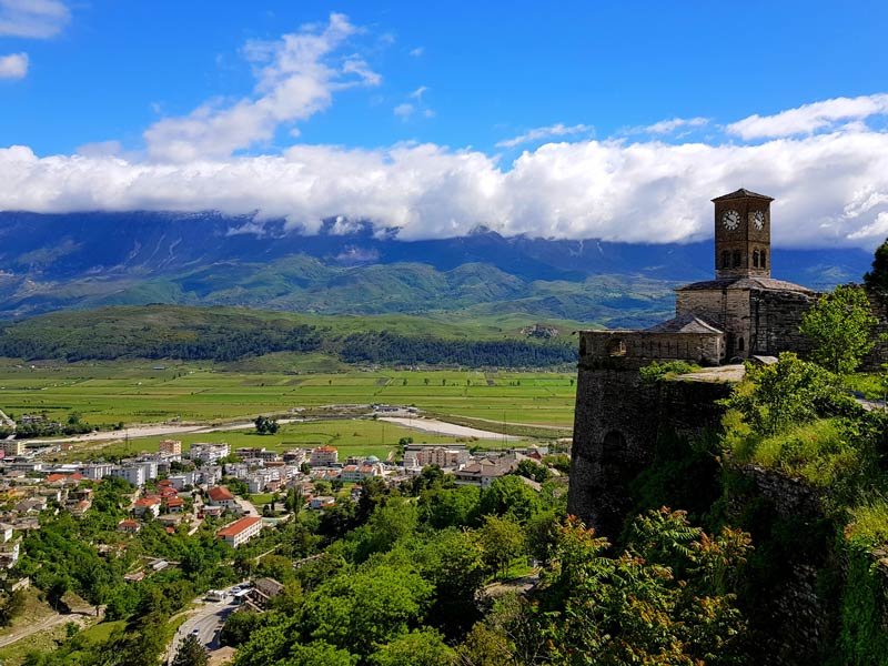 Historische stenen klokkentoren op een fort in Gjirokastër in Albanië met uitzicht op een stad, groene vallei en bergen met wolken