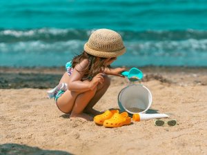 Kind met strohoed dat speelt met een schep en emmer op een zandstrand aan zee in Kroatië