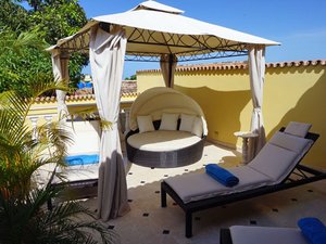Zonnig buitenterras met een wit prieel boven een rond ligbed en ligstoelen in Cuba