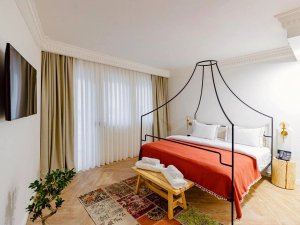Stijlvolle hotelkamer met hemelbed, oranje sprei en grote ramen met gordijnen in Pristina in Kosovo