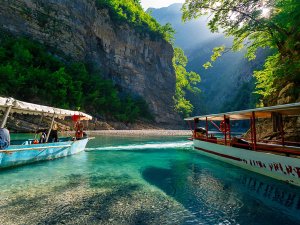 Twee boten op een heldere turquoise rivier in Albanië tussen zonnige kliffen en groene bomen