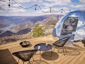 Moderne glamping dome met houten terras, zitplaatsen en vuurplaats, met uitzicht over een uitgestrekt bergmeer in de natuur bij Mavrovo in Noord-Macedonië
