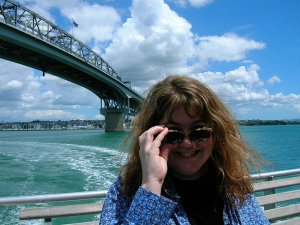 Lachende vrouw op een boot zet haar zonnebril recht met een grote brug en de stad over het water in Sydney Australië