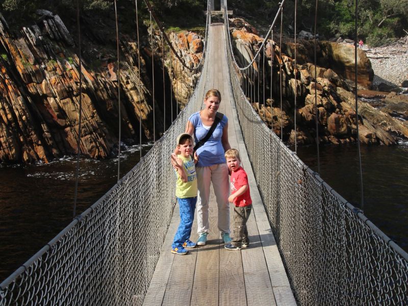 Vrouw en twee jonge jongens staan op een houten hangbrug boven een rivier met rotsachtige kliffen in Zuid-Afrika