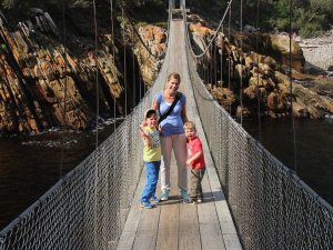 Vrouw en twee jonge jongens staan op een houten hangbrug boven een rivier met rotsachtige kliffen in Zuid-Afrika
