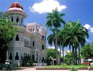 Sierlijk wit gebouw met rode koepel tussen hoge palmbomen onder een blauwe lucht bij Cienfuegos in Cuba