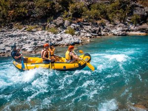 Four people rafting in a yellow boat on turquoise rapids.