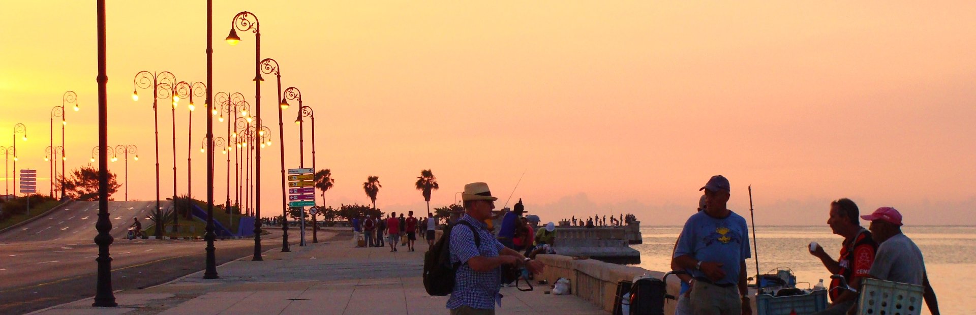 Boulevard aan zee bij zonsondergang met sierlijke lantaarnpalen, wandelaars en vissers langs het water in Cuba