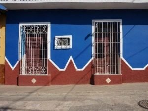 Felblauw gebouw met terracotta plint en witte zigzagdetails met drie ramen met witte tralies in Cuba