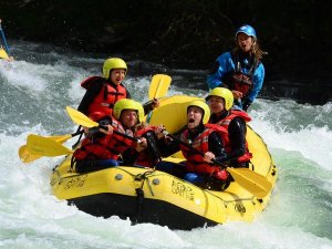 A yellow raft with five people in helmets and life vests navigates white water rapids.