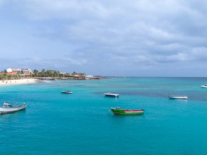 Boten drijven op fel turquoise water bij een zandstrand met een kustplaats op de achtergrond aan de kust