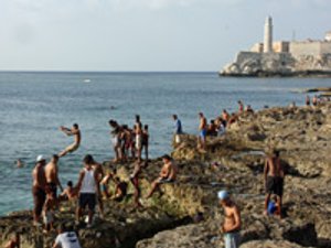 Mensen op een rotsachtige kust springen in zee met vuurtoren en fort in de verte in Havana Cuba