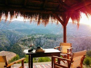 Tafel met wijn en boeken onder een rieten dak in Albanië met uitzicht op een bergkloof bij zonsondergang