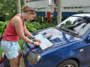 Vrouw leest een kaart op de motorkap van een blauwe auto tijdens een roadtrip in Viñales Cuba