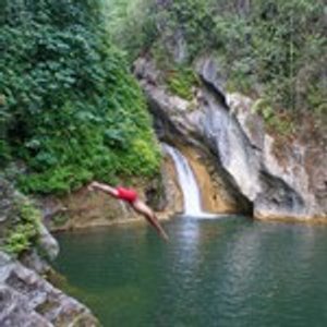 Persoon in rode shorts duikt in een groene natuurlijke poel met waterval in Topes de Collantes Cuba
