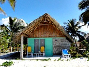 Tropische bungalow met rieten dak, teal deuren en terrasstoelen op een zandstrand met palmbomen bij Cayo Levisa in Cuba