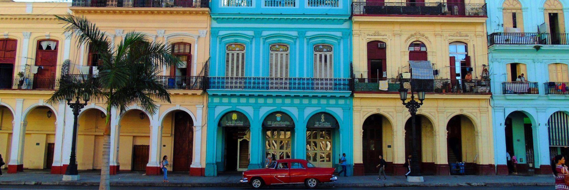 Levendige straat met kleurrijke gebouwen met bogen en een rode oldtimer en palmboom in Havana Cuba