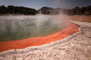 Stomende groene geothermische poel met een feloranje rand van mineraalafzettingen in een vulkanisch natuurgebied