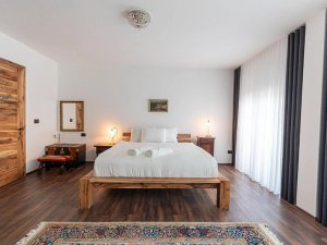 Lichte slaapkamer in Kosovo met houten bed, wit beddengoed, donkere houten vloer en kleurrijk patroonkleed