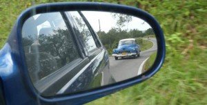 Reflectie in de zijspiegel van een auto van een vintage blauwe auto op een kronkelende weg in Cuba