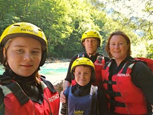 Gezin van vier met gele helmen en rode reddingsvesten bij een heldere blauwe rivier omringd door bomen in Kroatië