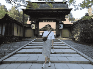 Iris die glimlachend poseert op de trappen voor de ingangspoort van een traditionele Japanse tempel.