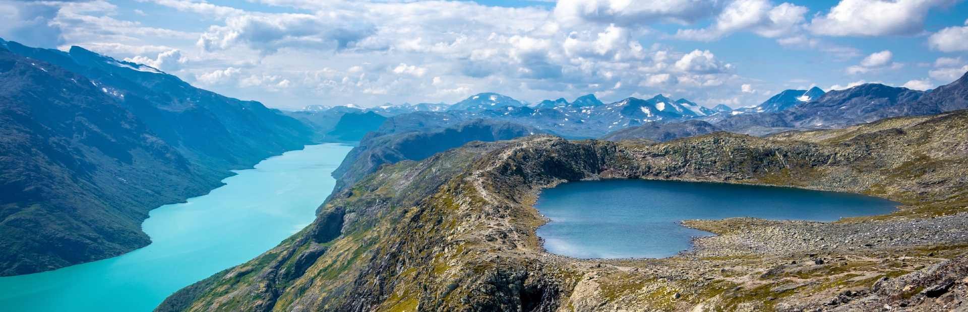 Panoramic mountain landscape with a long turquoise lake on the left and a smaller blue lake surrounded by rocky terrain on the right.