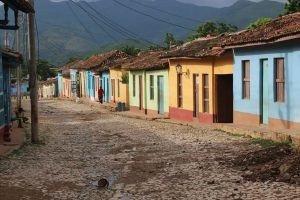 Kasseienstraat met kleurrijke koloniale huizen loopt richting bergen in de verte onder een bewolkte lucht in Cuba