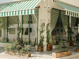 Gezellig terras met groen-wit gestreepte zonwering, grote ramen en zitplaatsen bij een hotel of café in Pristina in Kosovo
