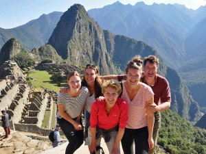 Groep van vijf mensen poseert lachend bij Machu Picchu met groene bergen op de achtergrond.
