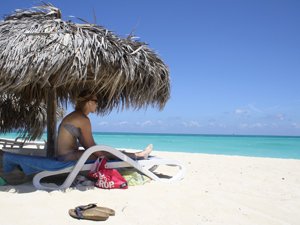 Vrouw onder een rieten parasol op een wit zandstrand in Varadero, Cuba met uitzicht op de turquoise oceaan