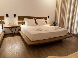 Moderne rustieke slaapkamer met bed van massief hout, wit beddengoed en houten nachtkastjes met wandlampen in Berat, Albanië