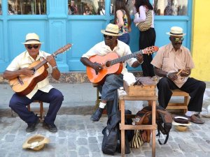 Drie straatmuzikanten spelen gitaren en percussie op een kleurrijke straat in Cuba