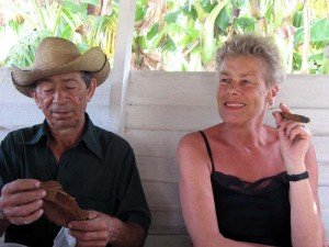 Oudere man met strohoed houdt tabaksbladeren vast naast een lachende vrouw met een brandende sigaar in Cuba