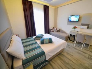 A bright, modern hotel room with a bed, chaise lounge, desk, and wall-mounted TV.