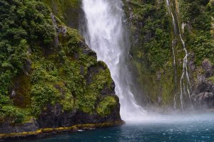 Waterval stort van een groene klif in blauw water met opstijgende nevel in een tropisch natuurgebied