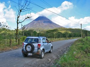 Auto rijdt over een landweg met uitzicht op de Arenal vulkaan in Costa Rica.