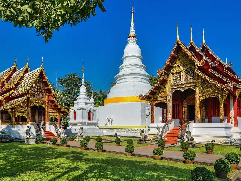 Witte stoepa en kleurrijke tempelgebouwen op een groene binnenplaats in Chiang Mai.