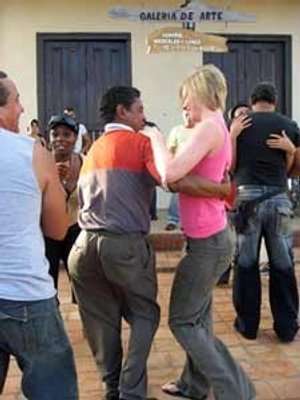 Lachende vrouw en man dansen salsa buiten met een groep mensen eromheen bij Viñales in Cuba