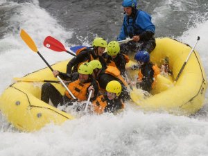 A group of people in a yellow raft paddle through whitewater rapids.