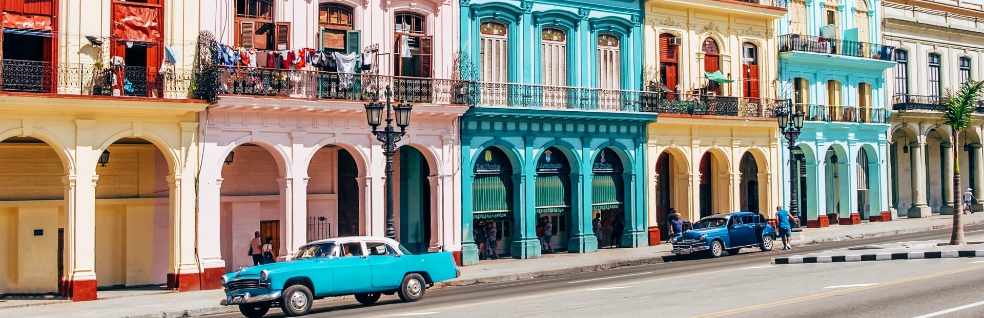 Levendige straat met kleurrijke koloniale architectuur en twee vintage auto’s in Havana in Cuba