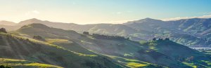 Panoramisch uitzicht op zonverlichte groene glooiende heuvels met mistige bergen en een wateroppervlak in de verte in een natuurgebied