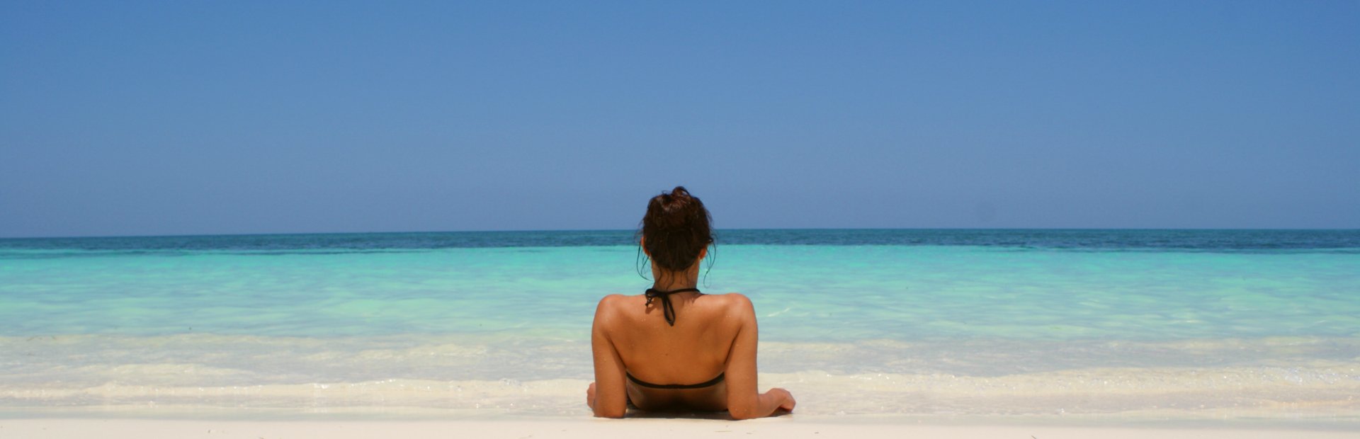 Een vrouw ligt op een wit zandstrand in Cuba en kijkt naar het turquoise zeewater onder een blauwe lucht.