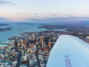 Luchtfoto van Auckland met haven en de Sky Tower bij schemering gezien vanaf een vliegtuigvleugel aan de kust in Nieuw-Zeeland