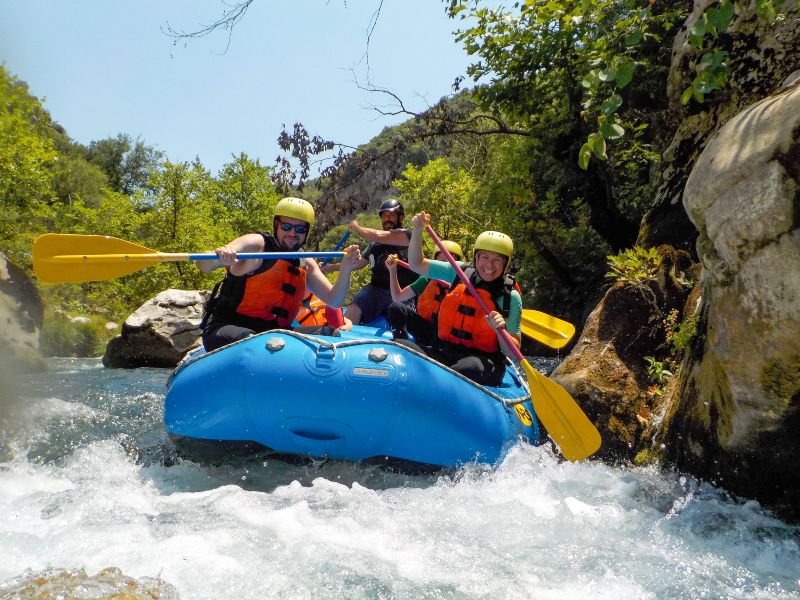 vier personen in blauw raft tijdens wildwaterraften door stroomversnellingen met helmen en reddingsvesten, Albanië