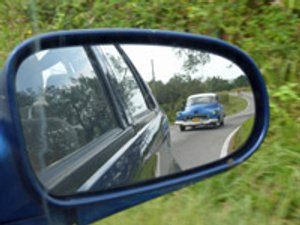Blauwe oldtimer weerspiegeld in een zijspiegel op een kronkelende weg in Viñales Cuba